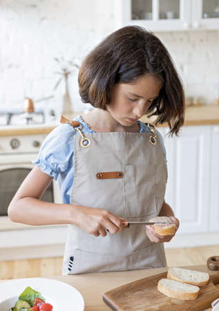 Cute brunette teen makes sandwiches in the domestic kitchen. Beautiful girl is cooking in the...