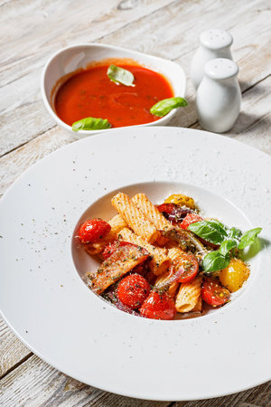 Close-up traditional penne pasta with tomatoes, spices, Parmesan cheese and fresh basil. Dish of classic Italian cuisine in a white plate on a wooden background. Vertical shot. Copy space. Top viewの写真素材