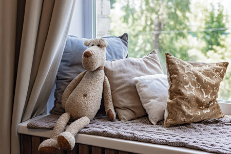 Soft toy bear. Various soft pillows and a knitted blanket on the windowsill. Children's room decoration. Home decorの写真素材