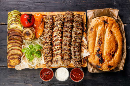 Assorted kebabs from different types of meat. Veal, chicken, lamb kebabs with vegetables and sauces on a wooden board. Traditional Turkish street food. Food delivery service concept. Top viewの写真素材