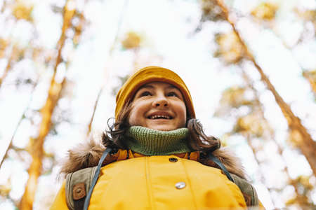 Portrait of a cheerful caucasian tourist girl in an orange jacket and hat. Hiking in the autumn...