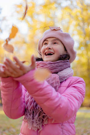 Portrait of a cute pretty happy smiling girl. Young attractive caucasian teenage girl walking in the autumn park. Leaf fall background. Vertical shot. Soft focusの写真素材