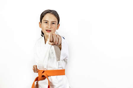 Karate girl on a white background. A sporty Caucasian laughing brunette in a white kimono is engaged in martial arts and practicing hand punches. Healthy lifestyle and self defense concept. Copy spaceの写真素材
