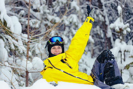 Cute happy young woman snowboarder in bright clothes makes funny pose in snowy snowboard park....
