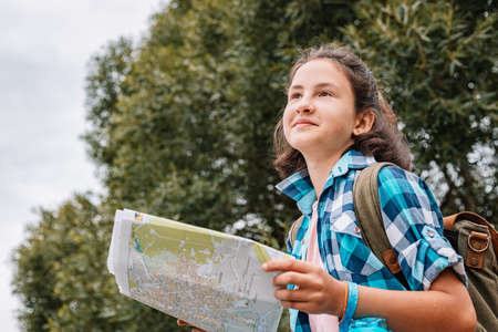 Cute teen girl travel in summer vacation. Hipster young girl with a backpack looks at a paper map....