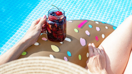 Beautiful women in the blue swimming pool. A woman's graceful hand holds a berry cocktail....