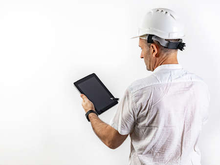 Male engineer in a white hard helmet. Middle-aged man in a white shirt with a tablet computer. back...
