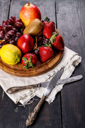 Assorted juicy ripe fruits. Strawberry, kiwi, apple, pear, banana, grapes. Delicious tropical fruits on a wooden background. Healthy breakfast concept. vertical shot. copy spaceの写真素材