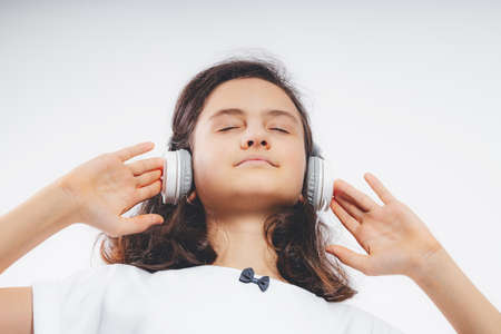 Photo of young happy beautiful caucasian teenager girl listen music in headphones on a white color background. Teenager stock photo. Beautiful brunette girl in a white T-shirt. close-upの写真素材