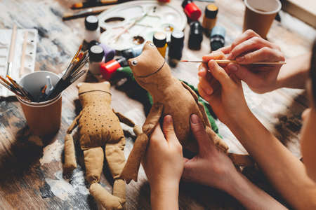 Hands of mother and child coloring handmade toy. Creativity together with kids. Process crafting a vintage toy. handmade frog dolls. DIY gift making. close-upの写真素材