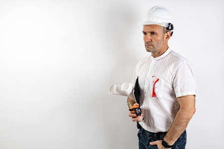 Male engineer in a white hard helmet. A middle-aged man in a white shirt, with blueprints and a...
