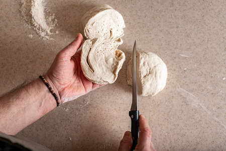 Male hands cut the dough with a knife. Human hands prepare dough for home baking. top view
