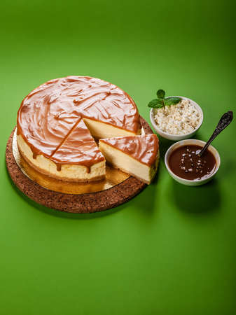 Classic cheesecake with salted caramel on a green background. Homemade delicious pastries. close-up. vertical shot. sweet dessert. copy spaceの写真素材