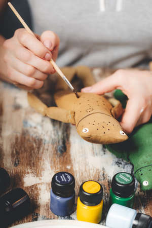 Handmade soft Doll frog. DIY gift crafting. Human hands hold frog soft toy. Needlework accessories on gray background. handmade house decor. Process of making a vintage soft toy. vertical shot.の写真素材