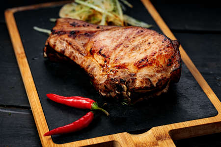 Grilled meat on a stone board. Appetizing grilled steak with herbs and spices. dark wooden...