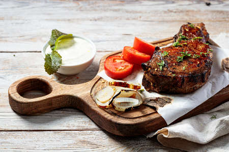 Grilled steak on a cutting board. Appetizing roasted meat with vegetables and herbs. copyspace. close-upの写真素材