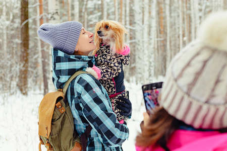 A teenager takes a photo on a smartphone of mom and dog. A woman is holding a Chinese Crested dog in her arms. Family walk outdoors in winterの写真素材
