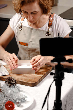 Woman making handmade chocolates and creates content for social media. Live broadcasts from the camera of a mobile smartphone of a master class on making sweets, chocolate truffles. vertical shotの写真素材