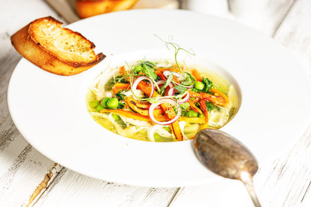 Appetizing vegetable soup with green peas, carrots, potatoes and garlic croutons. White wood background.の写真素材