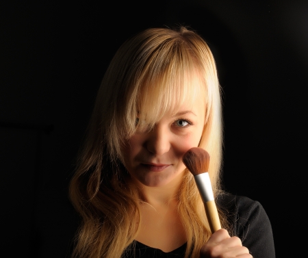 young blond hair woman portrait  with make-up brush on dark background.の写真素材
