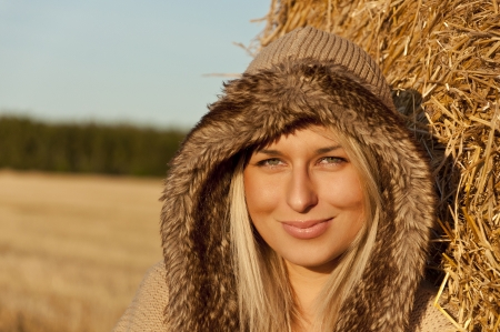 Beautiful young woman face. Winter clothing over wheat bale and field as backgroundの写真素材