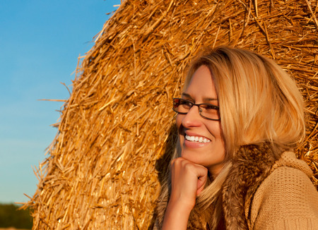 Beautiful young woman face. Winter clothing over wheat bale and field as background