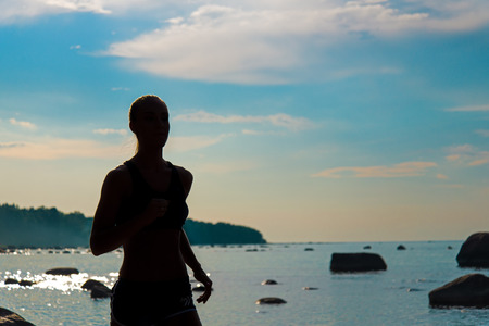 Running woman silhouette. Female runner jogging during outdoor workout on beach. Beautiful Fitness Model Outdoors.の写真素材