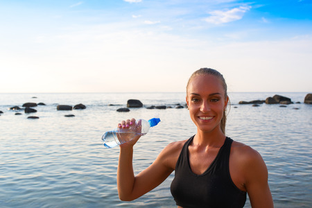 Young blond female in sports attire rests with water.の写真素材