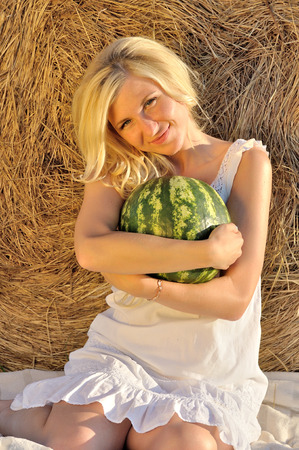 Happy woman posing with watermelon wearing white dress and hay as backgroundの写真素材