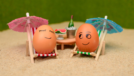 easter funny eggs sitting on a chair under umbrella on a sand and bottle of champain in a  bucket with watermelon. selective soft focusの写真素材