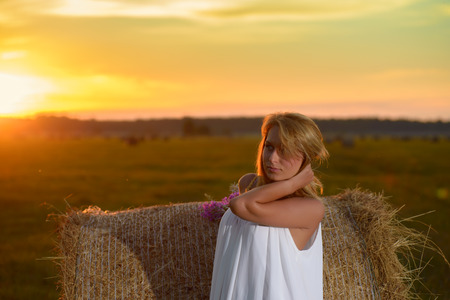 Blond woman posing at sunset time on a field with hayの写真素材