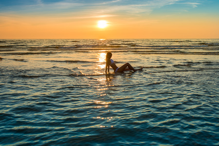 woman in white bikini posing in a sea at sunset timeの写真素材