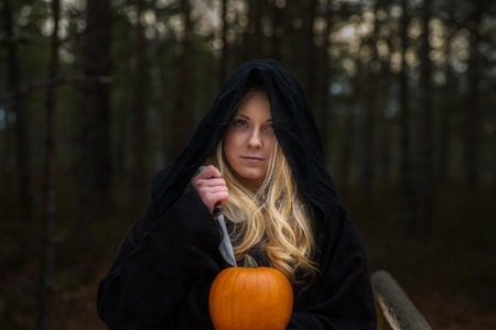 Young woman in Halloween witch costume in the autumn forest with yellow pumpkin.の写真素材