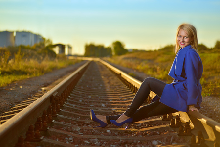 blond woman in blue coat posing on railraodの写真素材