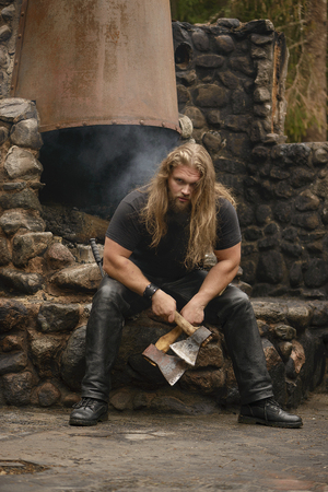 long hair Brutal man with axes near forest houseの写真素材