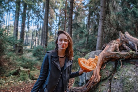 young beautiful woman in leather jacket with pumpkin in a forest