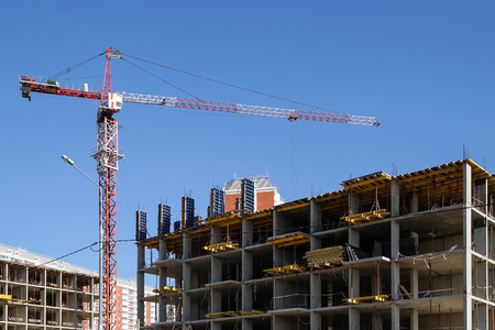 The tower crane builds a concrete house against the blue sky.の写真素材