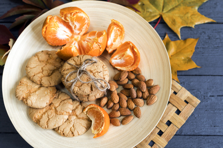 Tasty almond cookies on a wooden plate surrounded by autumn leavesの写真素材