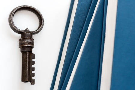 On a white table are collected paper books. Nearby there is an antique metal key. A symbol of knowledge and wisdom. Library archive.の写真素材