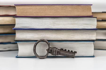 On a white table are collected paper books. Nearby there is an antique metal key. A symbol of knowledge and wisdom. Library archive.の写真素材