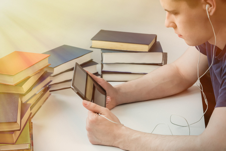 A young man is reading an e-book on the background of old paper books. The student is educated in the library.の写真素材