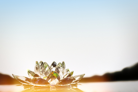 The glass lotus flower lies in the water. The rays of the sun shine. The stones in the background are in balance. Harmony and peace.の写真素材
