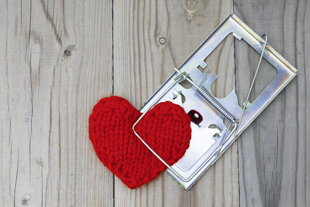 The red knitted heart is clutched by a mousetrap. The concept of fatal love. Difficult personal relationships.の写真素材