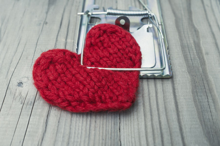 The red knitted heart is clutched by a mousetrap. The concept of fatal love. Difficult personal relationships.の写真素材
