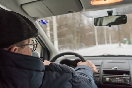 An elderly man is sitting at the wheel of a car. Winter, day.