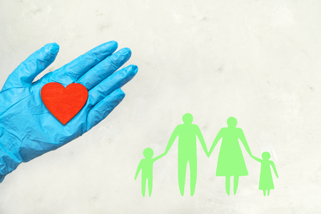 A hand in a medical glove holds a red heart. On a white background the contour of a family. Protection, insurance.の写真素材