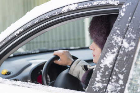 The girl is sitting at the wheel of a car. In the open window of the profile of the woman and the hand holds the steering wheel. Day, winter.の写真素材