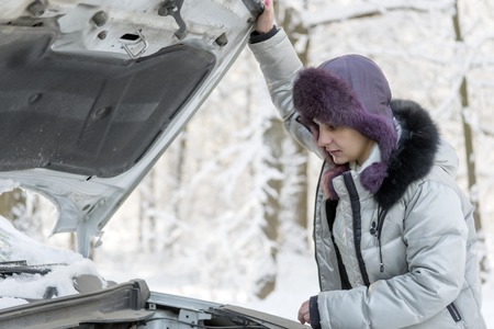 The girl lifted the hood from the car and looks at the engine. Winter, day.の写真素材