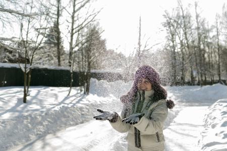 A woman holds a handful of snow in her hands and blows on it. Winter in the forest. The sun sparkles. Day, Russia.の写真素材