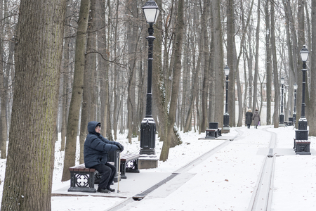 Man - elderly pensioner, sits on a park bench in the winter. High trees, a lantern. Tsaritsyno, Moscow.の写真素材
